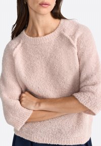 Pull oversized rose clair en tissu tricot doux et moelleux. Il présente un encolure ronde et des manches trois-quarts avec des poignets côtelés.