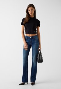 Zwarte cropped t-shirt, blauwe wijde jeans met een vervaagde effect, zwarte handtas en puntige zwarte hakken. Eenvoudig ontwerp zonder extra patronen.