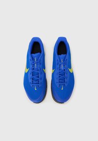 Modri atletski čevlji z mrežastim zgornjim delom, ki imajo rumene detajle in vezalke. Zaobljen špiček, teksturiran podplat in vidna blagovna znamka "Vaporfly".