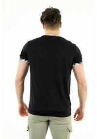 Sort kortærmet skjorte med hvidt trim på ærmerne og kraven. Glat stof, tætsiddende design, set fra ryggen, parret med lys grønne bukser.