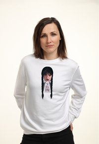 Mladá žena s hnědými vlasy, oblečená v bílém mikině se středovým potiskem dívky s černými copy a textem "NO HUG ZONE".
