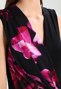 Black sleeveless dress featuring a deep V-neck; one side adorned with large, vibrant pink floral print, soft texture.