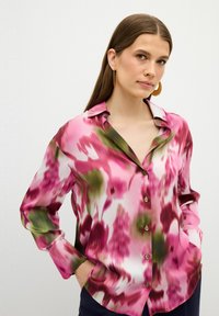 Camisa de seda de botones con un estampado floral en tonos rosa y verde, mangas largas y cuello en pico. Textura suave con un corte relajado.