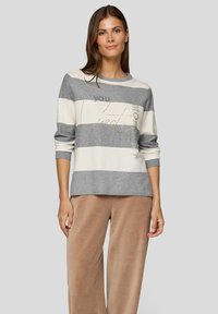 Grau-weiß gestreifter Pullover mit rundem Ausschnitt, langen Ärmeln und goldener Textdetail. Kombiniert mit weiten beigen Cordhose.