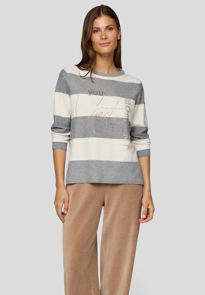 Grau-weiß gestreifter Pullover mit rundem Ausschnitt, langen Ärmeln und goldener Textdetail. Kombiniert mit weiten beigen Cordhose.
