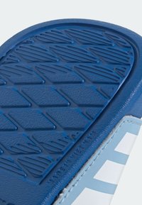 Blå gummisula med texturerat greppmönster. Ovandelen har en slät ljusblå sektion med vita ränder och synliga sömmar.