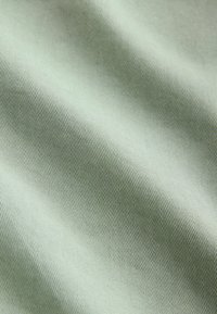 Tissu vert clair lisse avec une fine texture nervurée diagonale et de doux plis créant des ombres délicates.