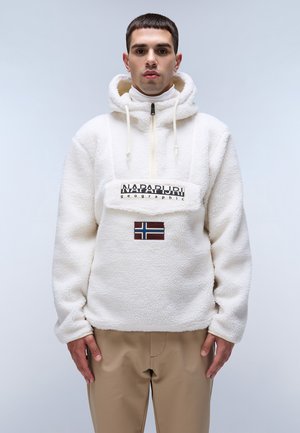 Hvid fleece-pullover med halvlukning, snoretræk i huen, har et logo-patch foran og et norsk flag-ornament. Sammen med beige bukser.