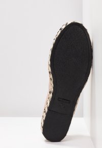 Semelle en caoutchouc noire d'une chaussure plate avec des côtés tissés de style espadrille sur fond blanc.
