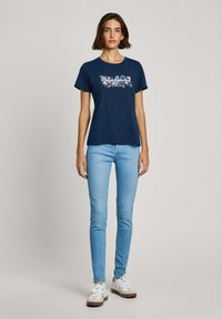 T-shirt en coton bleu marine avec un motif floral en blanc et rose. Associé à un jean skinny bleu clair et des baskets blanches avec des accents marron.