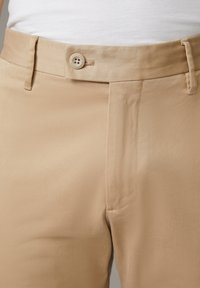 Beige Hosen aus einem glatten, leichten Stoff; verfügen über einen Knopfverschluss und dezente Nähte entlang des Bundes.