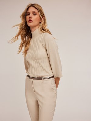 Top de punto acanalado beige con cuello alto y mangas hasta los codos, combinado con pantalones beige a medida y un cinturón metálico como acento.