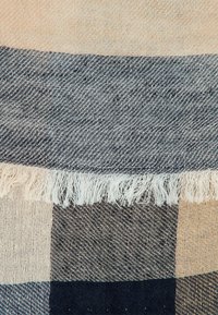 Beige, sort og mørkegrå ternet vævet stof med en frynset kantdetalje.