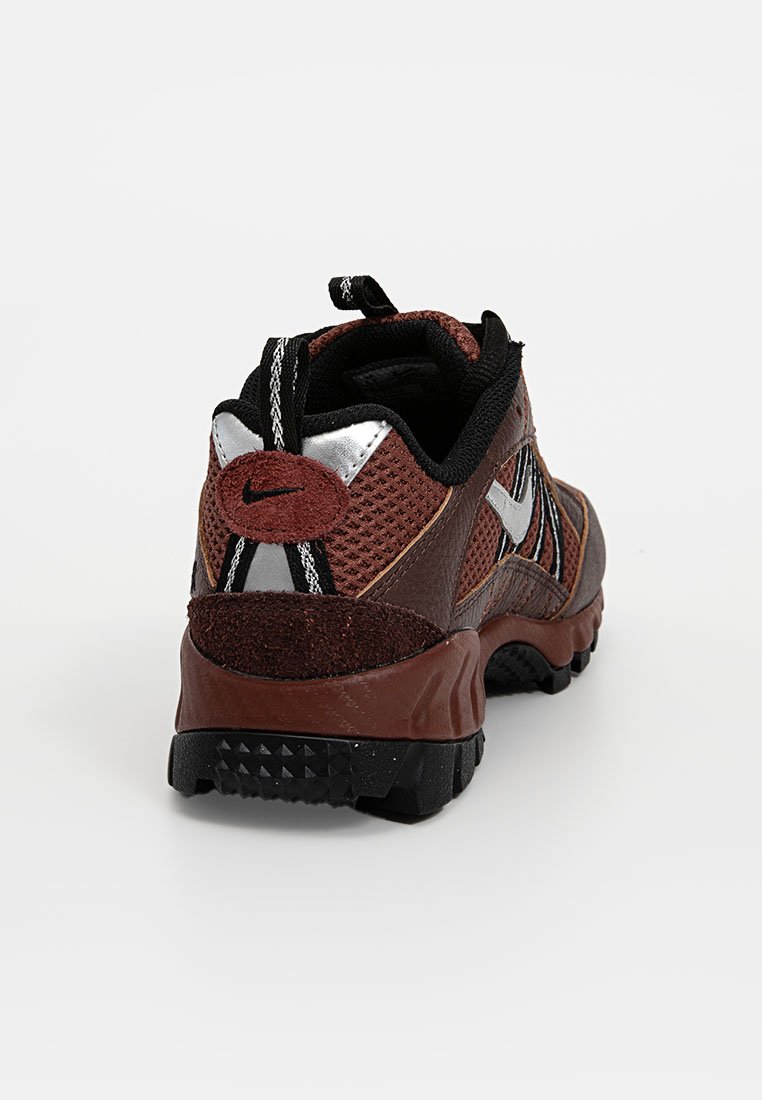 Chaussure Nike en marron et noir avec un dessus en mesh, des accents en daim et des détails argentés. Dispose d'une semelle texturée et d'une languette à l'arrière pour faciliter l'enfilage.
