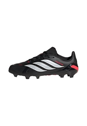 Czarny but piłkarski z białymi paskami Adidas, czerwonym akcentem na pięcie oraz korkami na podeszwie zapewniającymi przyczepność na trawie.