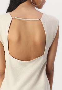 Bagdel af en lys beige linnedkjole med en bred udskæring, lille lynlås og uden ærmer. Glat, struktureret stof.