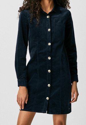 Granatowa sukienka koszulowa z sztruksu, z długimi rękawami, dwoma kieszeniami na piersi i srebrnymi guzikami z przodu. Gładka faktura i długość do kolan.