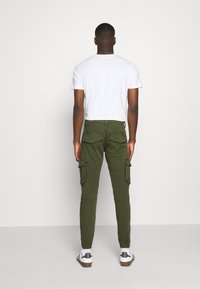 Olivgröna cargobyxor med sidofickor, smal passform och synliga sömmar, i kombination med en enkel vit T-shirt och vita sneakers.