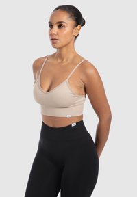 Beige geribde bralette met dunne bandjes en een v-hals, gecombineerd met hoge zwarte leggings. Bevat een klein logo detail op de tailleband.