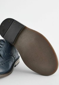 Marineblå lædersko med vinge-design. Har en tekstureret brun gummisål og en let hæl, samt dekorative perforeringer og syninger.