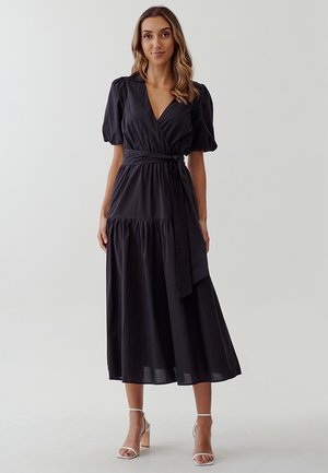Black wrap dress with short puff sleeves, a tie belt at the waist, and a tiered skirt. Made from a lightweight, smooth fabric.