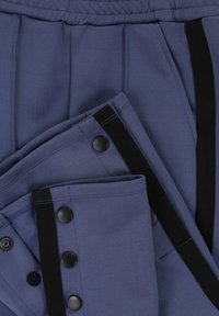 Marineblauwe broek met een gladde textuur, voorzien van zwarte knopen en accenten, plooien bij de taille en een ontspannen pasvorm.