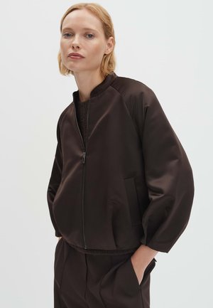 Giacca bomber in tessuto marrone, liscia, con cerniera, colletto alla coreana, tasche laterali e maniche leggermente imbottite. Design minimale, colore uniforme.