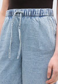Ανοιχτό μπλε τζιν παντελόνι με ελαστική μέση, κορδόνι και υφή φινιρίσματος. Σχεδιασμένο για άνετη εφαρμογή.