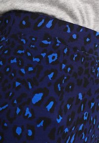 Blå leopardmönstrad tyg med svarta accenter, som har en slät yta. Materialet verkar stretchigt, lämpligt för åtsittande plagg.