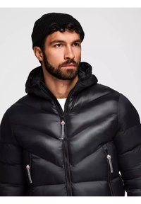 Giubbotto puffo nero con motivo a chevron, chiusura frontale con zip e tasche laterali. Dotato di cappuccio e texture liscia e lucida.