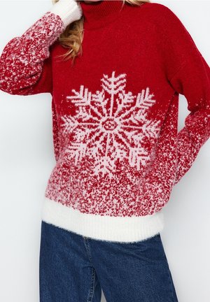 Röd stickad tröja med ett vitt snöflingemönster, texturerat material och vita ribbade muddar och nederkant. I kombination med blåjeans.