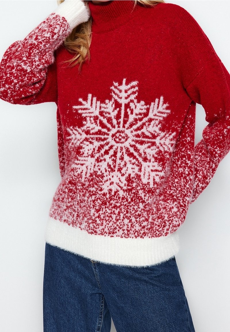 Punainen neulepaita, jossa on valkoinen lumihiutalevaurio, teksturoitu materiaali ja valkoiset ribbauskäänteet ja helma. Yhdistetty sinisiin farkkuihin.