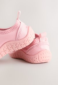 Coppia di morbide scarpe rosa per bambini con suola in gomma texturizzata e linguette per tirare su, su sfondo chiaro.