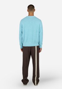 Šviesiai mėlynas pūkuotas megztinis su ilgomis rankovėmis, dėvimas su tamsiai rudos spalvos kelnėmis, turinčiomis baltą šoninių juostą. Aprangos atbulas vaizdas.