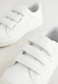 Hvide sneakers med en glat syntetisk læderoverflade, der har tre velcrosløjfer og en struktureret gummisål.