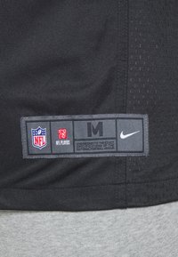 Sort stof med syet rektangulært mærke, der viser NFL, NFL Players logoer, størrelse M og hvid Nike swoosh på struktureret baggrund.