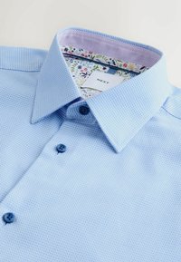 Svetlomodrá košeľa na gombíky s textúrovaným vzorom. Kontrastný kvetinový vzor vo vnútri goliera a modré gombíky. Viditeľná značka výrobcu.