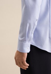 Camicia azzurro chiaro con texture e design aderente. Presenta un colletto a punta, polsini con bottoni e un sottile motivo diagonale. Tessuto morbido.