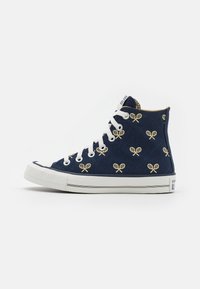 Baskets montantes en toile marine avec des lacets blancs, présentant un motif matelassé et des accents de raquette de tennis jaunes. Capuchon en caoutchouc à l'avant et semelle.