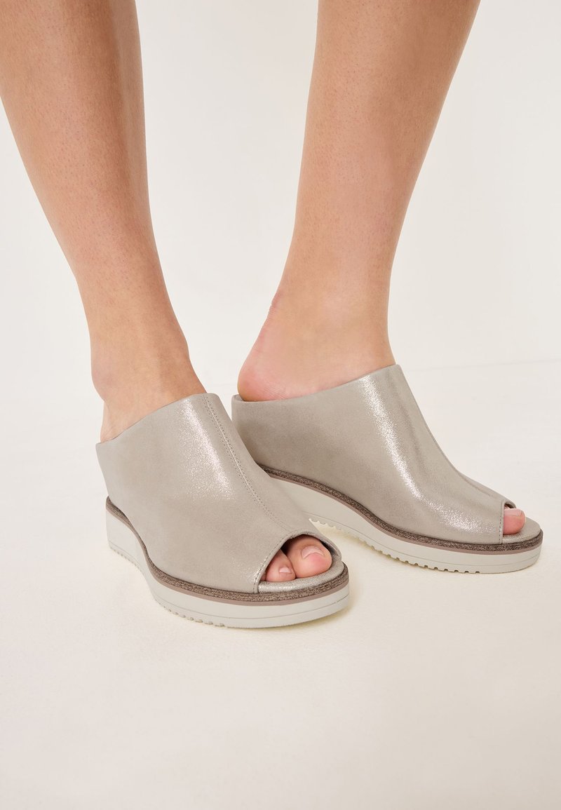 Mules de cuña en cuero gris claro con un acabado brillante; diseño de punta abierta; suela de goma blanca; textura suave y lisa con un estilo minimalista.