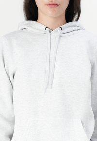 Lys grå hettegenser laget av myk stoff, har en frampocket, snorer i hetten og et enkelt, avslappet fit-design.