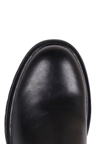 Gros plan sur l'avant d'une chaussure en cuir noir avec une surface lisse et polie et des coutures détaillées le long du bord sur fond blanc.