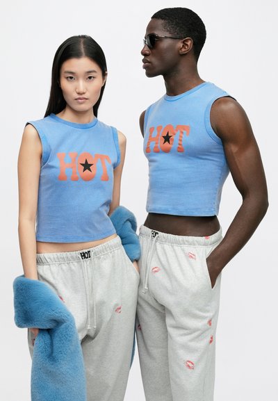 Top azul curto sem mangas com estampa laranja "HOT" e estrela, combinado com calças de treino cinzentas com padrões de beijos. Detalhe em pêlo azul.
