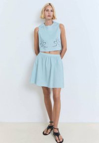 Top corto azul claro con detalles de lazo bordados en ojal y bordes en forma de concha, combinado con una falda acampanada a juego que presenta una cinturilla elástica.