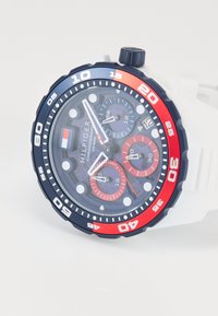 Tommy Hilfiger chronograph watch with white strap, blue and red bezel, three subdials, and date display at 4 o'clock.