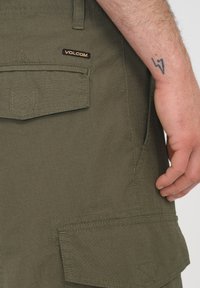 Zielone oliwkowe szorty cargo z teksturowanej tkaniny, widocznymi kieszeniami i logo Volcom. Zawierają dekoracyjne przeszycia na tkaninie.