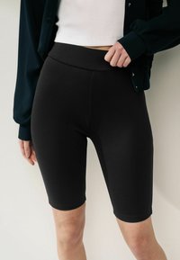 Czarne szorty rowerowe wykonane z elastycznego materiału z wysokim stanem, charakteryzujące się gładkimi szwami i dopasowanym krojem sięgającym do połowy uda.