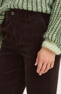 Braune Cordhosen mit glatter Textur, einer Druckknopfverschluss und Taschen. Kombiniert mit einem grünen, grob gestrickten Pullover.