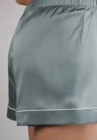 Světle šedé šortky vyrobené z hladké tkaniny, s elastickým pasem a bílým kontrastním lemem. Navrženy pro volný střih.