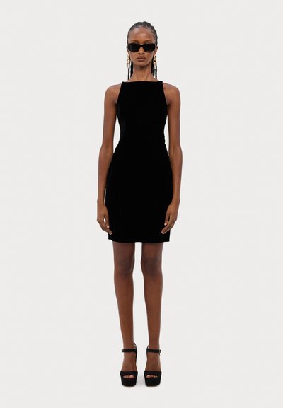 Rochie mini neagră din catifea, cu o siluetă ajustată, decolteu larg și cusături laterale subtile. Purtați cu tocuri înalte negre și ochelari de soare supradimensionați.